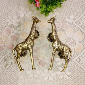 Puede incluir: Un par de tiradores de puerta de jirafa de color dorado con un patrón de manchas. Los tiradores están hechos de metal y tienen un diseño detallado.