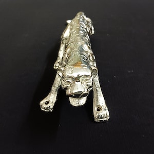 Könnte beinhalten: Eine silberfarbene Metallfigur eines Leoparden mit detailliertem Design und einem knurrenden Ausdruck.
