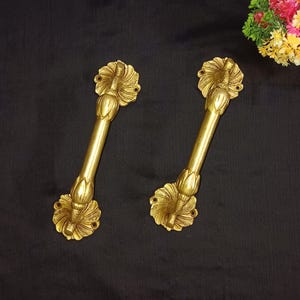 May include: Two ornate gold door handles with a floral design. The handles are made of brass and have a polished finish.
