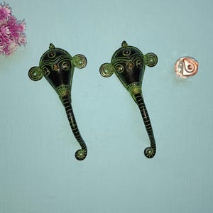 以下が含まれることがあります： 複雑なディテールが施された象の頭の形をした黒と緑の金属製のドアノブが2つ。ノブは湾曲したデザインで、薄い青色の壁に取り付けられています。