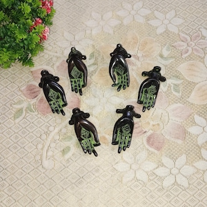 Op de afbeelding: Zes antieke messing deurgrepen in de vorm van handen met ingewikkelde groene ontwerpen. De grepen zijn in een cirkel op een witte achtergrond gerangschikt.