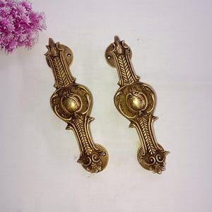 May include: A pair of ornate brass door handles with intricate floral designs. The handles are a gold color and have a traditional style.