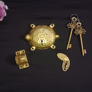 Puede incluir: Un juego de cuatro piezas de herrajes para puertas de metal dorado. El juego incluye un llamador de puerta con forma de tortuga, una tapa para el ojo de la cerradura, una manija de puerta y dos llaves esqueleto.