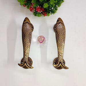 Könnte beinhalten: Zwei goldfarbene, fischförmige Türklinken mit detaillierten Schuppen und einer strukturierten Oberfläche.