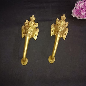 May include: Two gold-toned door handles with intricate elephant head designs. The handles are ornate and feature a crown-like design on top of the elephant heads.