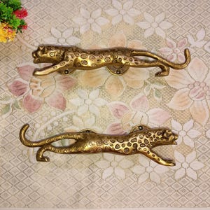 May include: Two gold-toned leopard door handles. The handles are detailed with a leopard print pattern and have a realistic leopard shape.