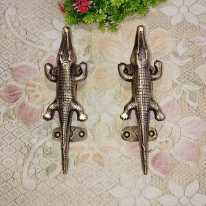 Peut inclure: Une paire de poignées de porte en laiton antique en forme de crocodile. Les poignées sont détaillées avec des écailles texturées et ont un design de crocodile réaliste.