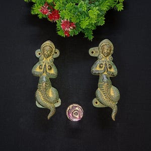 Peut inclure: Deux poignées de porte antiques en laiton représentant une divinité avec un corps de serpent. Les poignées ont une finition verte et dorée vieillie. Un petit bouton rond rose et violet est également présent.
