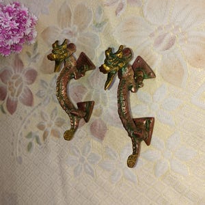 May include: Two antique brass dragon door handles with a green and gold patina. The handles are shaped like dragons with their heads facing forward and their tails curled around the handle.
