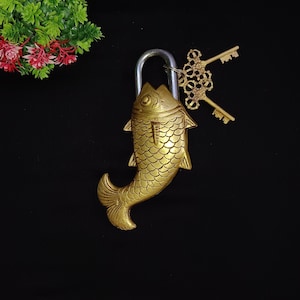 Può includere: Un lucchetto in ottone dorato a forma di pesce con due chiavi. Il lucchetto ha un anello in metallo argentato.