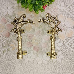 May include: A pair of gold-toned metal door handles with a parrot perched on a tree branch design. The handles are detailed with intricate carvings and have a rustic, antique look.
