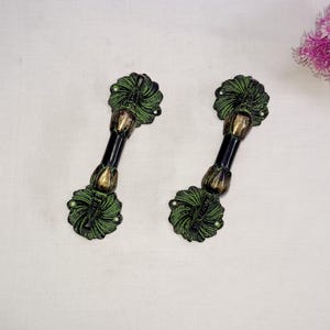 Puede incluir: Dos tiradores de puerta ornamentados en negro y verde con un diseño floral. Los tiradores son de metal y tienen un acabado pulido.