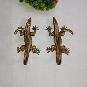 Peut inclure: Deux crochets en métal doré en forme de lézard. Les crochets sont conçus pour ressembler à un lézard avec sa queue enroulée. Les crochets sont parfaits pour accrocher des clés, des serviettes ou d'autres objets.