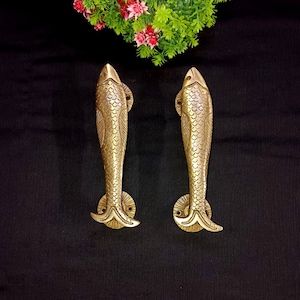 Könnte beinhalten: Ein Paar goldfarbene, fischförmige Türklinken. Die Griffe sind mit Schuppen verziert und haben eine runde Basis.