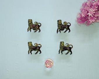 Puede incluir: Cuatro figuras decorativas de leones en tonos dorados y marrones están dispuestas sobre una superficie azul claro. También hay un pomo de cristal redondo y transparente y flores rosas. Las figuras de leones tienen detalles.