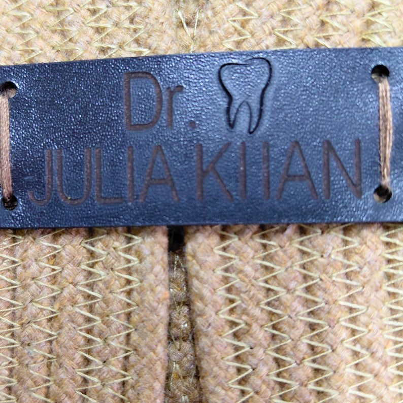 May include: A close-up of a dark blue leather tag with the text "Dr. Julia Khan!" and a tooth graphic. The tag is stitched to a woven, tan fabric.