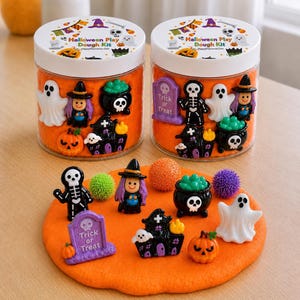 May include: Two clear plastic jars filled with orange play dough, topped with labels reading Halloween Play Dough Kit. The jars contain miniature Halloween-themed figurines including ghosts, witches, pumpkins, cauldrons, and tombstones.