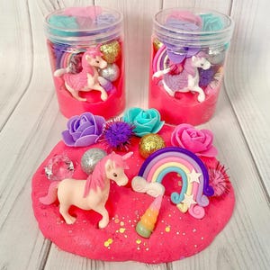 Peut inclure: Pâte à modeler rose avec des décorations de licorne et d'arc-en-ciel, des paillettes et des fleurs décoratives. Deux pots remplis de pâte à modeler rose, de licornes et de décorations arc-en-ciel. Un kit de bricolage amusant et coloré.