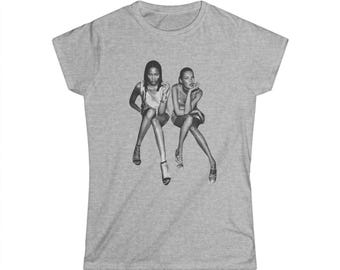 May include: A heather grey t-shirt featuring a black and white image of two women sitting with their legs crossed.