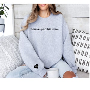 May include: A gray sweatshirt with the text "There's no place like home" and a small heart with the number 203 on the sleeve.