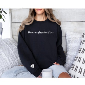 Puede incluir: Sudadera negra con el texto "There's no place like home" y un pequeño corazón con el número 305 en la manga.