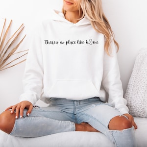 May include: White hoodie with a front pocket and the text "There's no place like home" in black script. The hoodie is worn with light blue jeans.