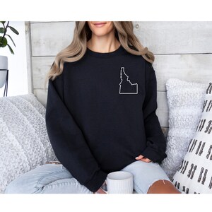 May include: Black sweatshirt with a white outline of the state of Idaho on the left chest. The state outline includes the abbreviation "ID" inside.