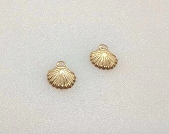 May include: Two small gold-toned metal charms shaped like scallop shells. Each charm features a textured, fan-like ribbed pattern radiating from a central point and includes a small circular loop at the top for attachment to jewellery or accessories.