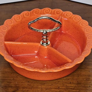 May include: Orange ceramic serving dish with three sections and a gold metal handle. The dish has a scalloped edge and a speckled glaze.