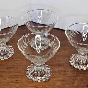 May include: Four clear glass dessert dishes with a delicate etched leaf design and a beaded base.