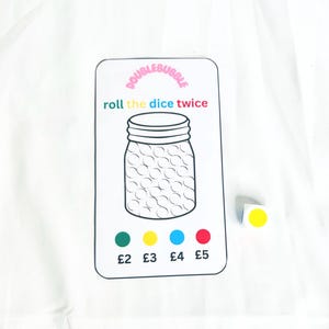 Può includere: Un cartoncino bianco con le parole "Double Bubble" in lettere rosa. Il cartoncino ha un'illustrazione in bianco e nero di un barattolo con un coperchio. Il testo "roll the dice twice" è scritto in lettere colorate. Sotto il barattolo ci sono quattro cerchi colorati con il testo "£2", "£3", "£4" e "£5" sotto. Un dado giallo è seduto su una superficie bianca a destra del cartoncino.