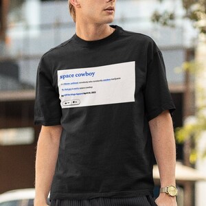 May include: A person wearing a black t-shirt with the text "space cowboy" and a definition of the term. The person is wearing black pants, a black cap, and sunglasses.