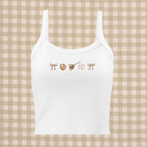 Pode incluir: Top branco de alças com um gráfico temático de beisebol. O gráfico inclui um taco de beisebol, uma bola de beisebol, uma luva de beisebol e dois laços.