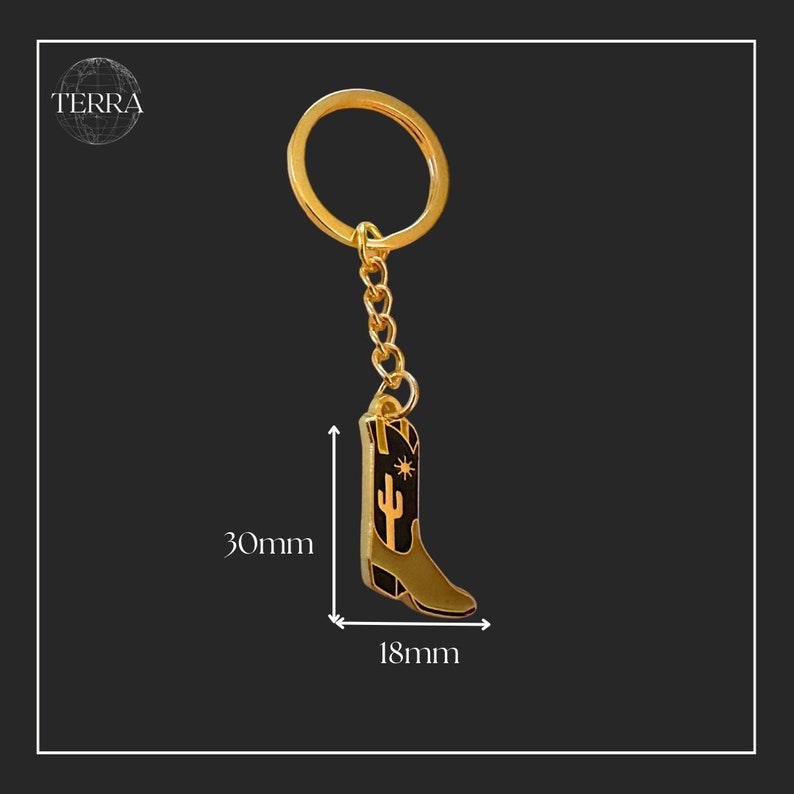 May include: Gold-tone metal cowboy boot keychain with a black enamel finish. The boot features a cactus and star design. The keychain measures 30mm in height and 18mm in width.