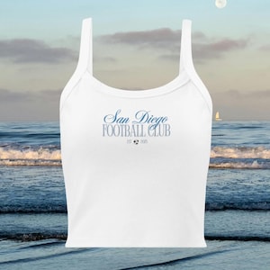 May include: White tank top with spaghetti straps. The text "San Diego Football Club" is printed in blue script, with "EST 2005" below. The top is set against a scenic ocean backdrop.