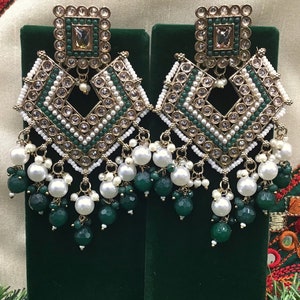 May include: A pair of gold-tone earrings with a square design. The earrings feature white pearls, green beads, and clear rhinestones.
