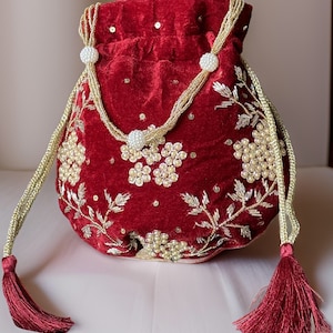 May include: A red velvet drawstring bag with gold embroidery and pearl accents. The bag has two long tassels.