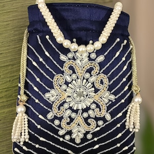 May include: A navy blue drawstring bag with a pearl and gold beaded design. The bag has a pearl tassel and a pearl strap.