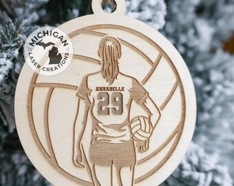 May include: A wooden volleyball ornament with a silhouette of a player holding a volleyball. The ornament is engraved with the text "Annabelle 29" and the logo "Michigan Laser Creations".