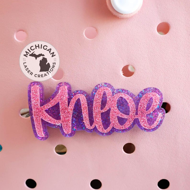 May include: Pink and purple glitter name tag with the name "Chloe" written in a cursive font.