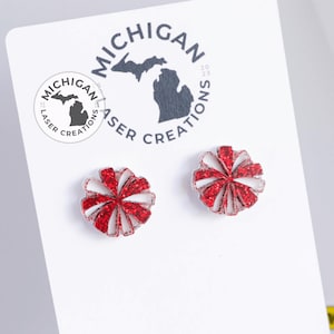 May include: A pair of red and white glitter pom-pom earrings. The earrings are on a white card with the text "Michigan Laser Creations 2023".