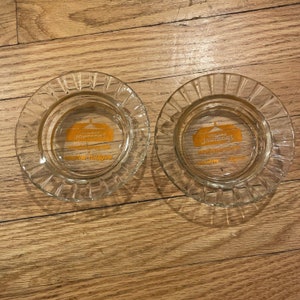 May include: Two clear glass ashtrays with a gold design. The design features the words "Howard Johnson's" and "motor lodges".