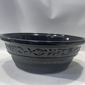 May include: A black ceramic bowl with a decorative floral pattern around the rim. The bowl has a ribbed texture on the lower half and a smooth, glossy finish. The bowl is designed for serving food.