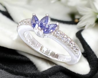 May include: A silver ring with a cluster of three purple amethyst stones set in a flower shape. The ring is adorned with a row of small clear stones.