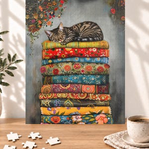 May include: A jigsaw puzzle featuring a brown tabby cat sleeping on a stack of colorful, patterned fabric textiles. The stack includes various floral and geometric designs in shades of red, blue, green, and yellow. The puzzle is set against a gray background with hanging floral vines at the top.