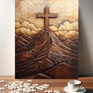 May include: A wooden jigsaw puzzle depicting a cross atop a mountain, with rays of light emanating from behind. The puzzle is mostly assembled, with some pieces scattered on a wooden surface. A white teacup and saucer are also on the surface.