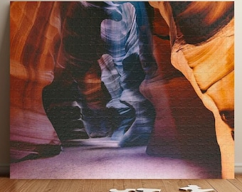 Könnte beinhalten: Fertiges Puzzle mit einer Canyon-Szene in Orange-, Lila- und Blautönen. Einige Puzzleteile liegen auf einem Holzboden vor dem Puzzle.