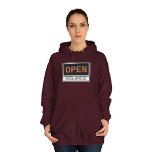 Puede incluir: Una sudadera con capucha color burdeos con un gráfico rectangular en blanco y negro que dice "OPEN SOURCE" en texto naranja.