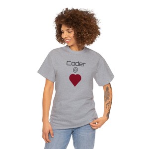 Könnte beinhalten: Hellgraues T-Shirt mit dem Text "Coder @" über einem roten Herz. Das Shirt besteht aus einem weichen Material und eignet sich für Freizeitkleidung. Das Design ist schlicht und auffällig, perfekt für Programmierer.