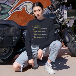 May include: A navy blue sweatshirt with a code snippet printed on the front. The code snippet is written in a light pink, yellow, and green font. The code snippet reads: "int favoritePuppy = 3; // Named "White Puppy" String[] favoritePuppy = { "Bullmastiff", System.out.println("Komondor"); 3: System.out.println("Labradoodle"); 4: System.out.println("Rottweiler"); "